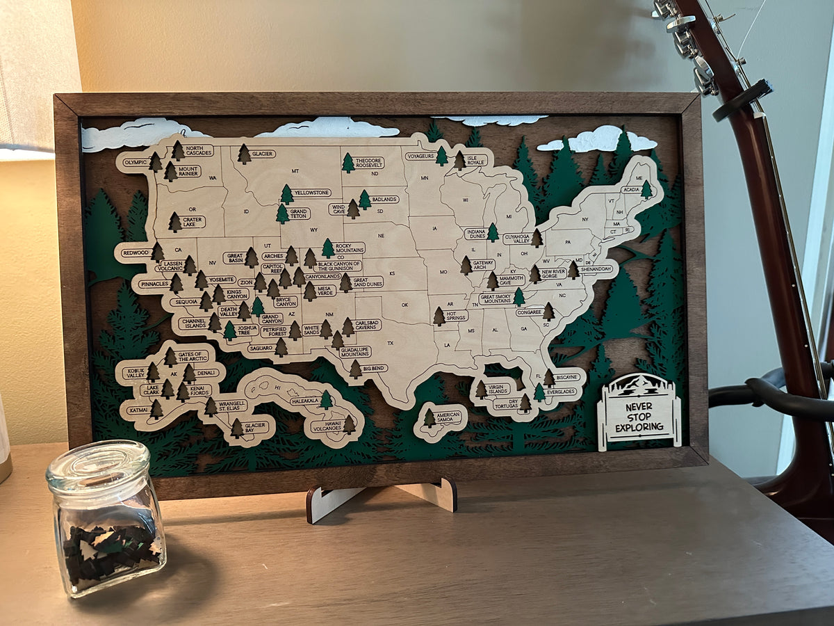 Map of United States with tree and skyline background. Every state with a National Park has tree cut out including Hawaii and Alaska that you can place back inside the cut out after your visit.